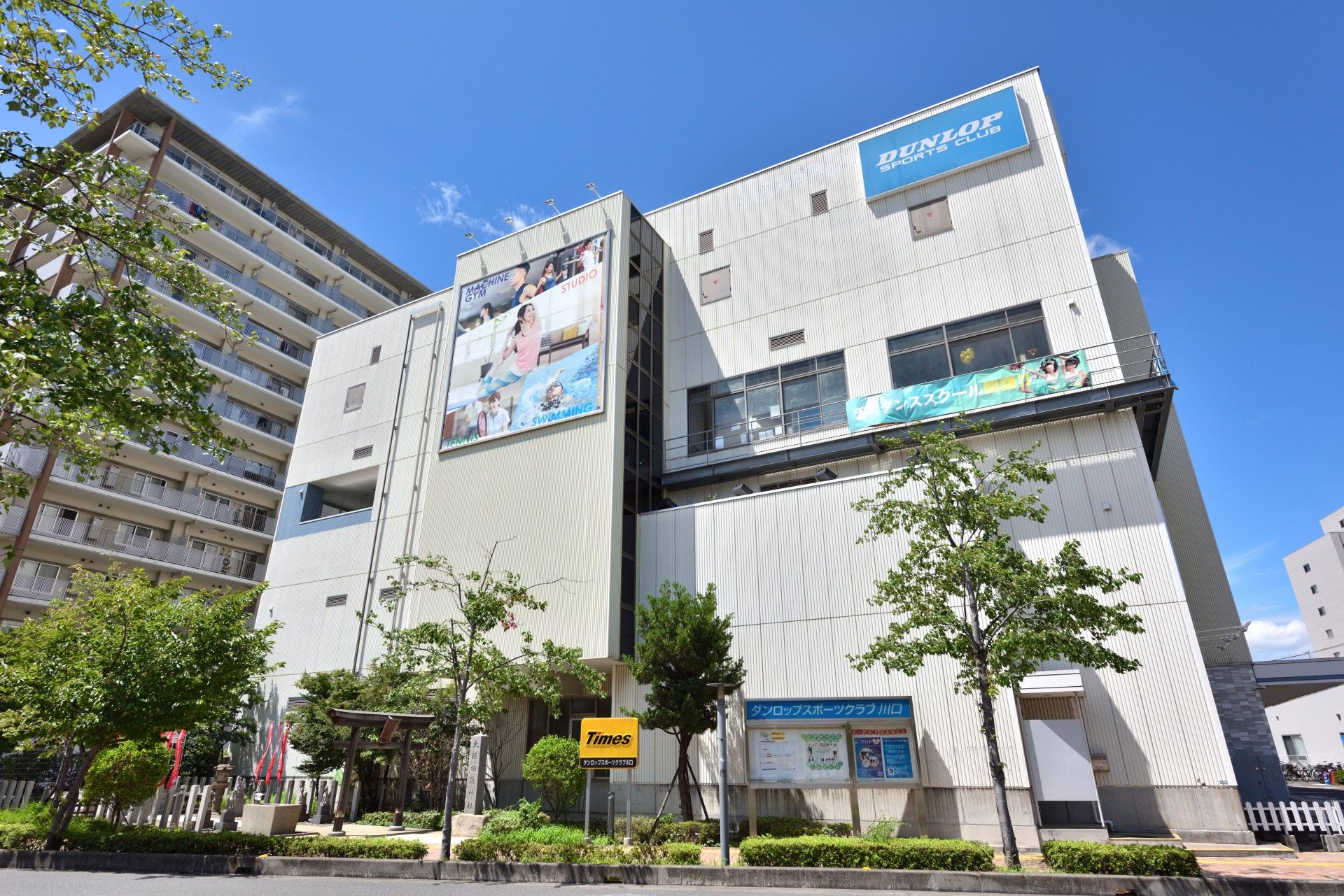 赤色と緑色のコントラストが印象的なコンビニがある。出入口のところに朝刊が置かれている。公衆電話もある