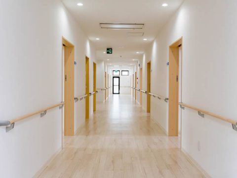 両サイドに手すりと居室のドアが設置されているまっすぐな廊下。突き当りに窓がある。