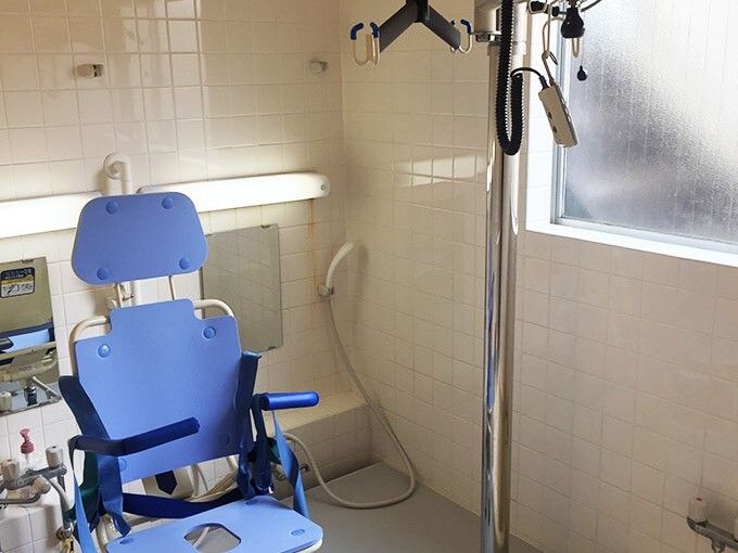 シャワーが付いた浴室の一角にリフトを持ち上げる用具があり、ブルーのリフトが設置されている。