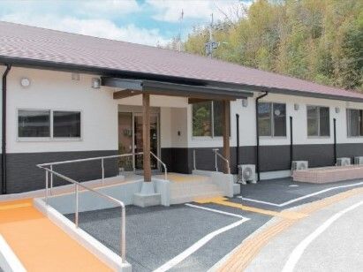 自然に囲まれた立地にあり、平屋建ての建物の玄関先には手すり付きのスロープと階段がある。