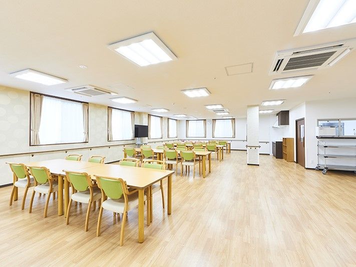 グリーンの椅子とベージュの机の組み合わせ、大型テレビがある広い空間