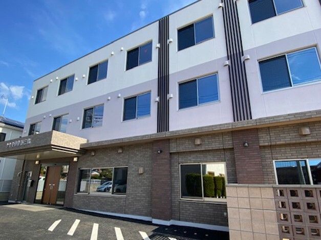 駐車場が付いた3階建ての建物は横に長く、玄関には屋根があり、日当たりも良好。