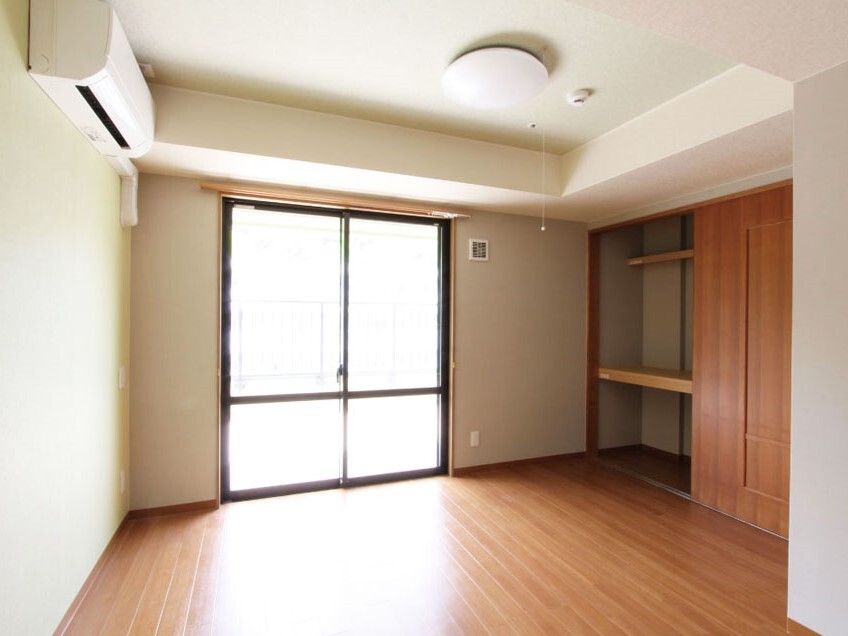 エアコン付きのフローリングの部屋には棚が付いた大きな収納スペースがあり、カーテンのない窓もある。