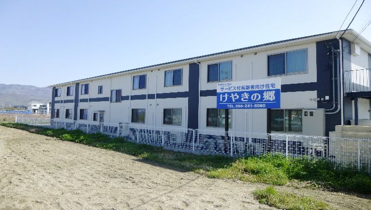 屋外で笑顔で過ごしている車いすの高齢女性と付き添いの高齢男性、若い男女のスタッフ。