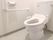 エル字型の手すりが付いた広いトイレにはふたのない便座が付いた洋式のトイレがある。