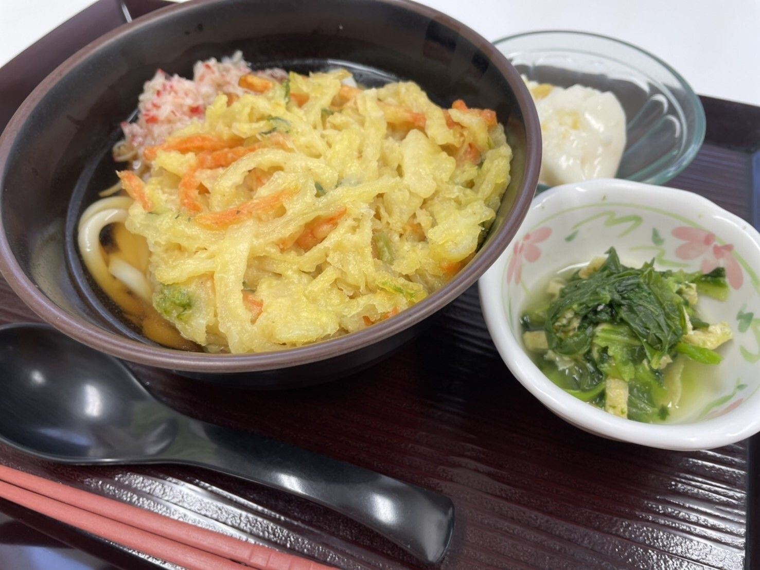大きなかき揚げが乗ったうどんの横には青菜のおひたしがあり、デザートも添えられている。