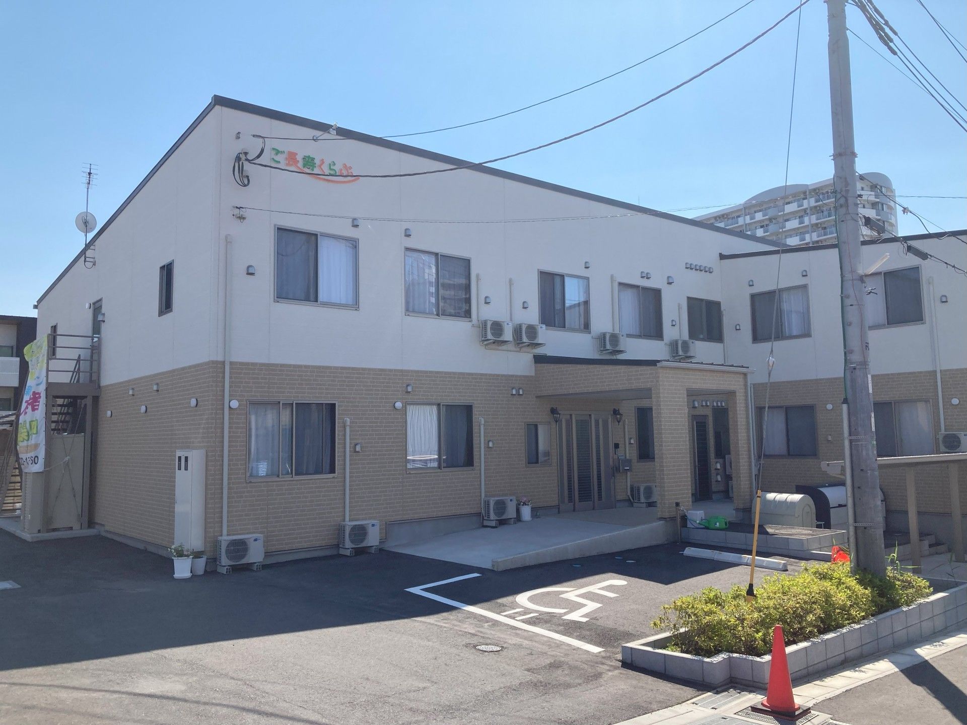 白とベージュの２階建ての建物は玄関に手すり付きのスロープがあり、側面に屋外階段も付いている。