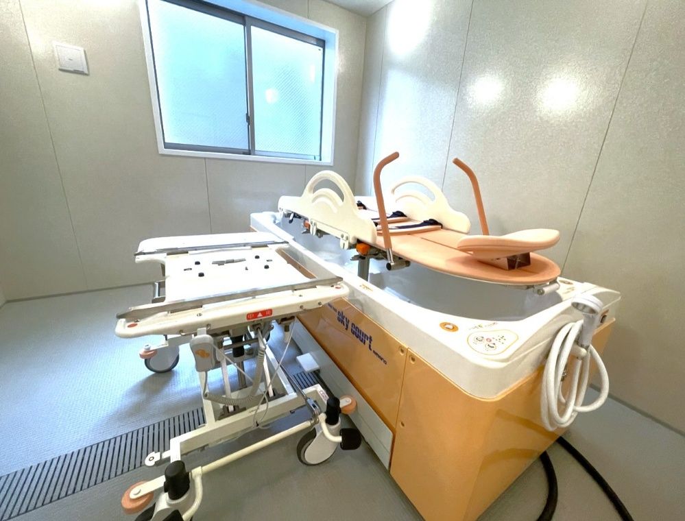 広い浴室内には白とピンクの座ったまま入浴可能な機械浴が設置されている。