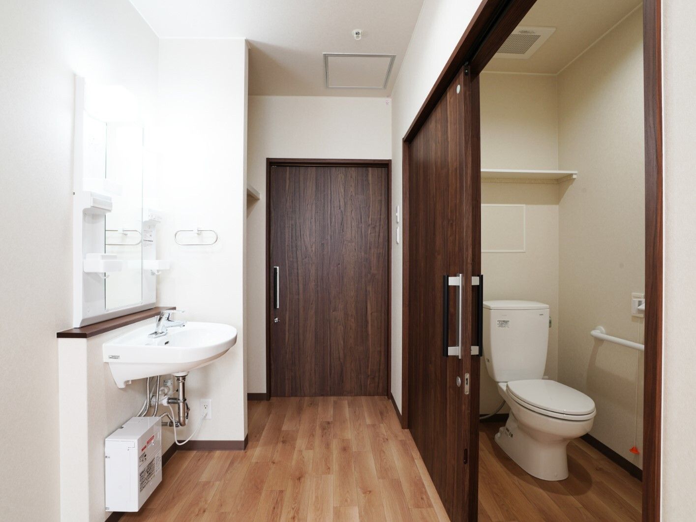 右側には手すりが付いたスライド式のドアが設置されたトイレがあり、左側には車いす対応の洗面所がある。