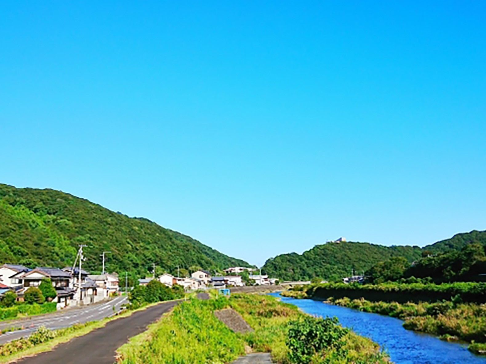 青空の下には山があり、民家が集まった場所と緑豊かな河川敷があり、川も流れている。