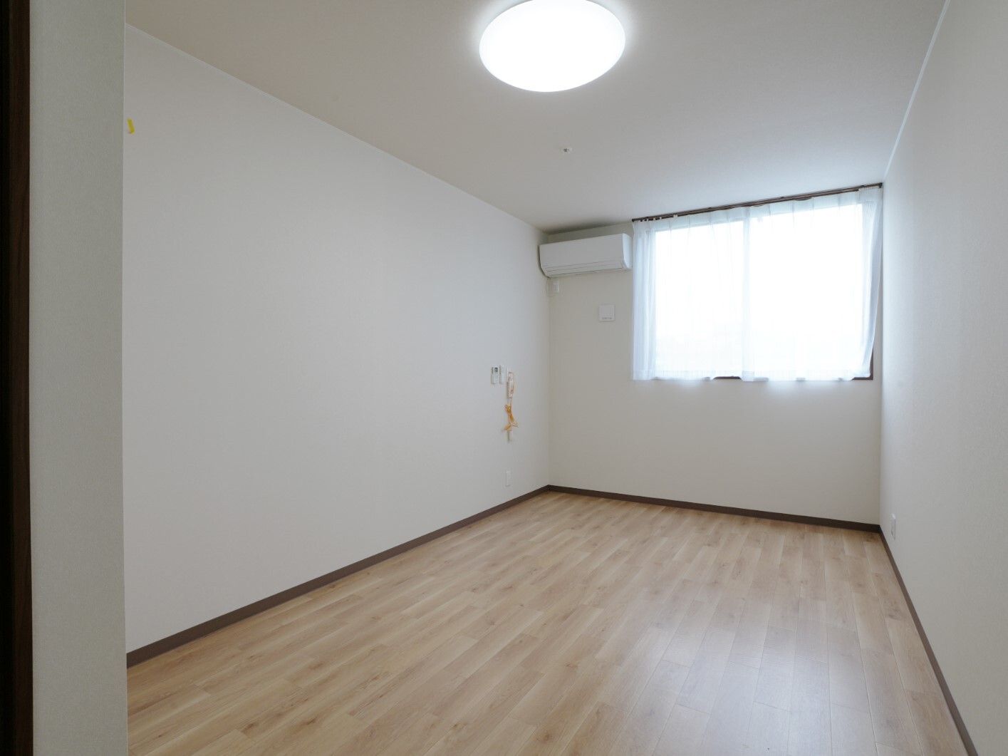 シンプルなフローリングの部屋にはエアコンや緊急通報装置があり、カーテン付きの窓もある。