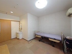 洗面所やエアコン、介護ベッドが置かれているカーペット敷きの部屋にはワイドタイプのスライド式のドアが設置されている。