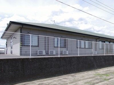 フェンスに囲まれた平屋建ての建物の周りには畑があり、日当たりのいい場所に建っている。