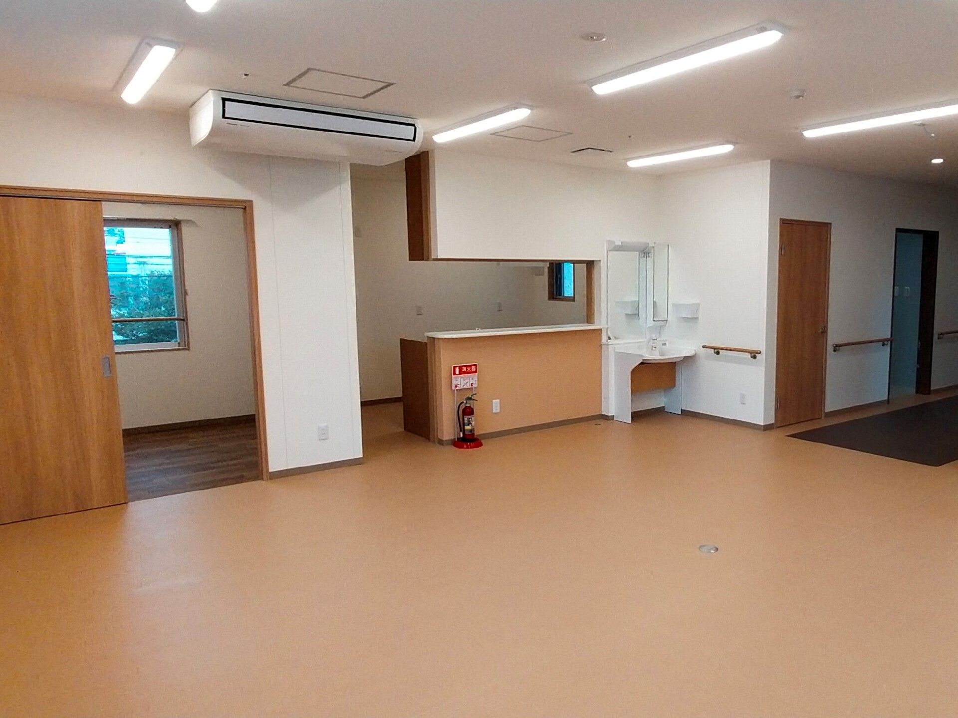 対面式のキッチンが付いたリビングダイニングには家具は置かれていない。消火器が設置されている。