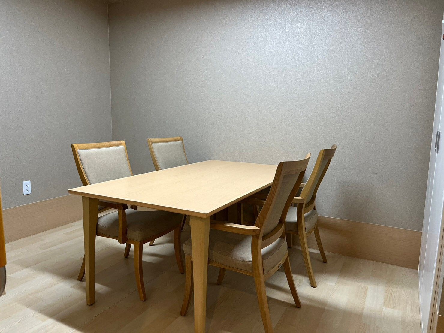 木製の4人掛けのテーブルセットが置かれている部屋はグレーの壁紙で、テーブルの上には何も置かれていない。