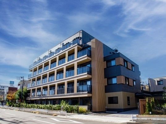 ダークグレーとベージュの外観の5階建ての建物の建っている敷地内には駐車場もある。