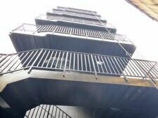 屋外階段が設置されたダークグレーの背の高い建物を下から見上げた様子。