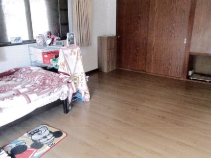 寝具付きのベッドが置かれ、収納スペースが付いたフローリングの部屋にはカーテン付きの窓もある。