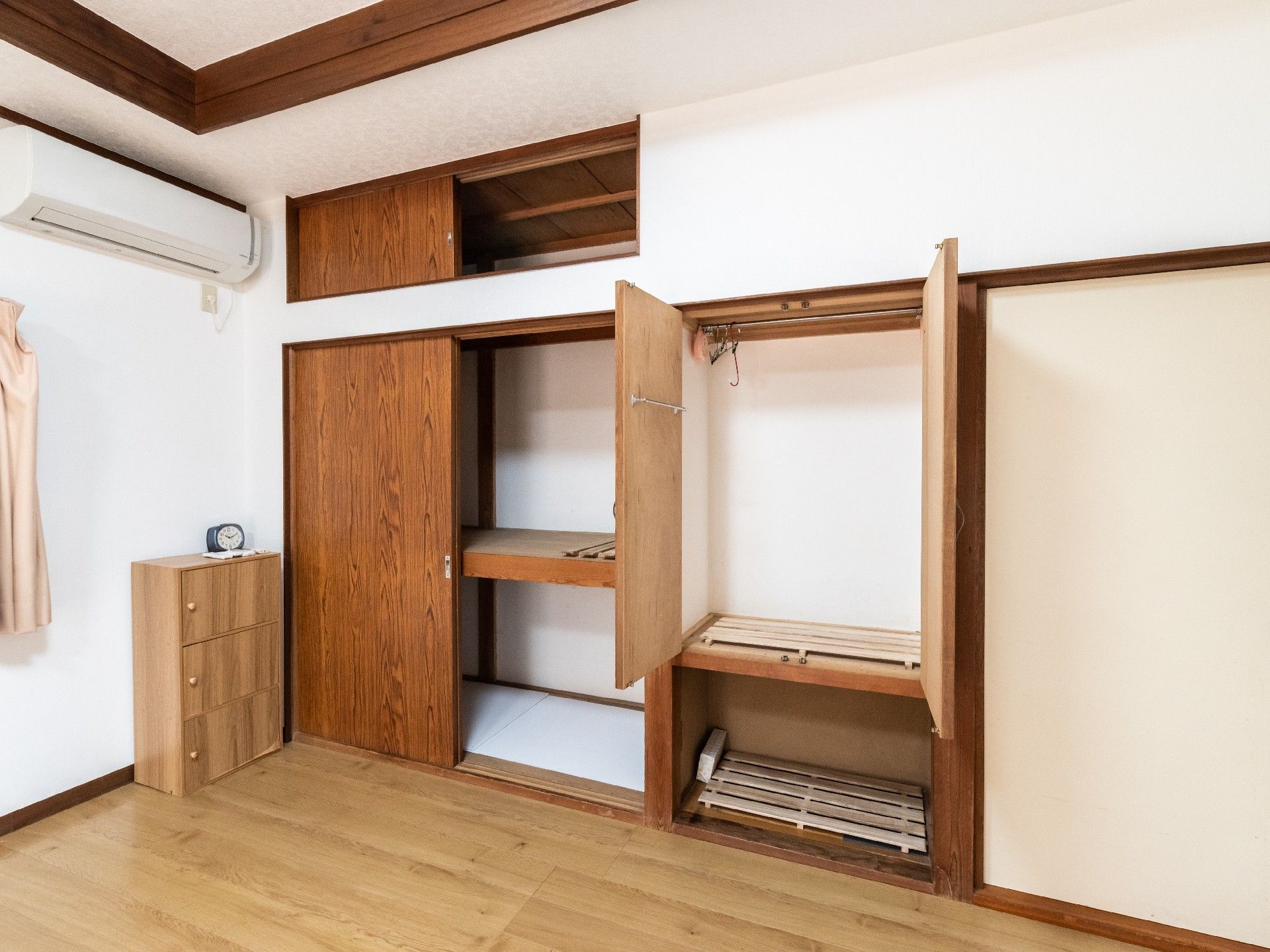 寝具付きのベッドが置かれ、収納スペースが付いたフローリングの部屋にはカーテン付きの窓もある。