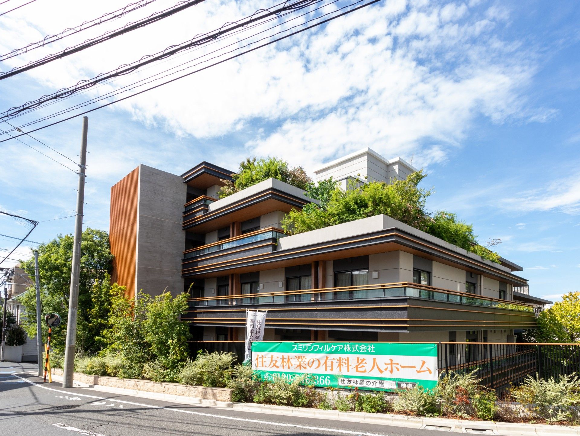 ベランダが付いたグレー系の大きな建物。ベランダや建物周辺には草木が植えられている。