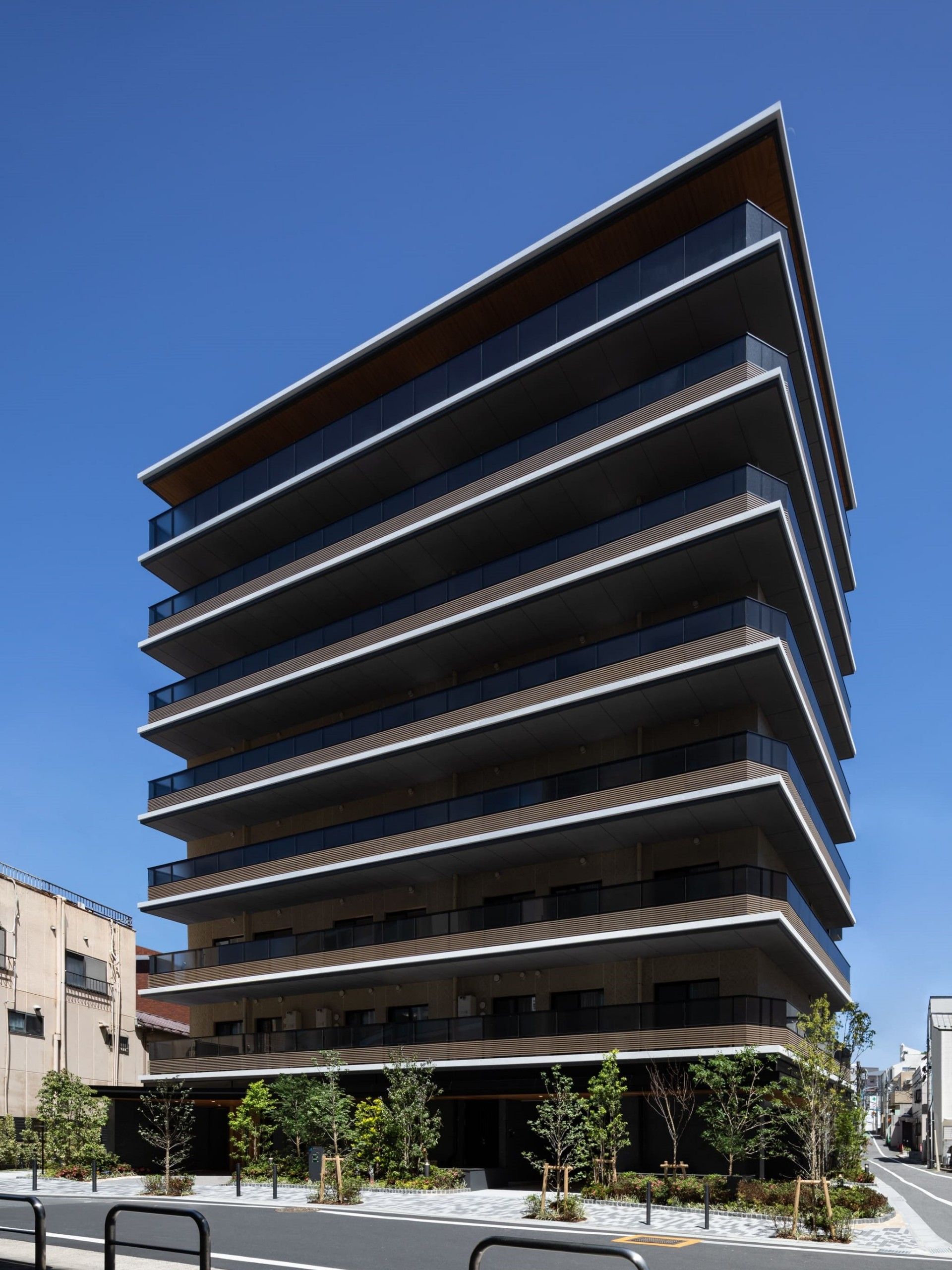 各フロアにベランダがあり、背の高いグレー系の建物の周りには草木が植えられている。