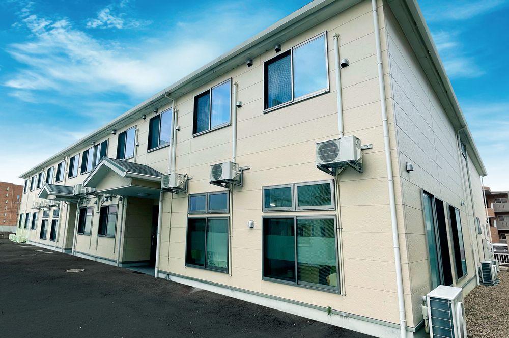 横に長い２階建ての建物は日当たり良好で玄関先には屋根が付いていて駐車場もある。