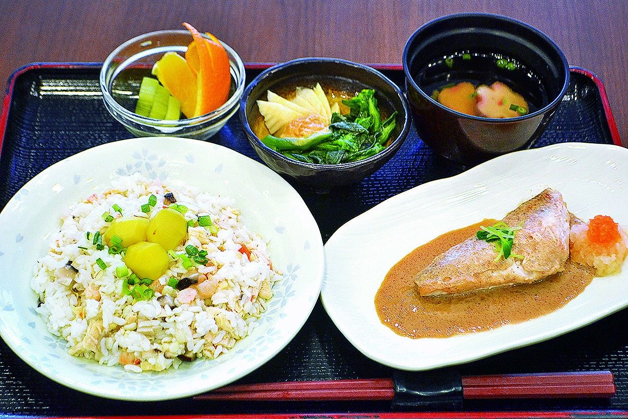 黒いトレーの上には肉や野菜が刻まれたおかずやおかゆ、具の入っていないみそ汁がある。