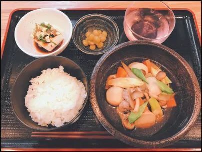 煮物や白いご飯、冷ややっこ、煮豆、デザートが並んでいる黒いトレーには箸も置かれている。