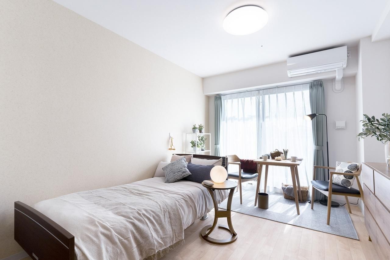 エアコンが付いたフローリングの部屋には寝具付きのベッドが置かれ、ベッドサイドには緊急通報装置がある。