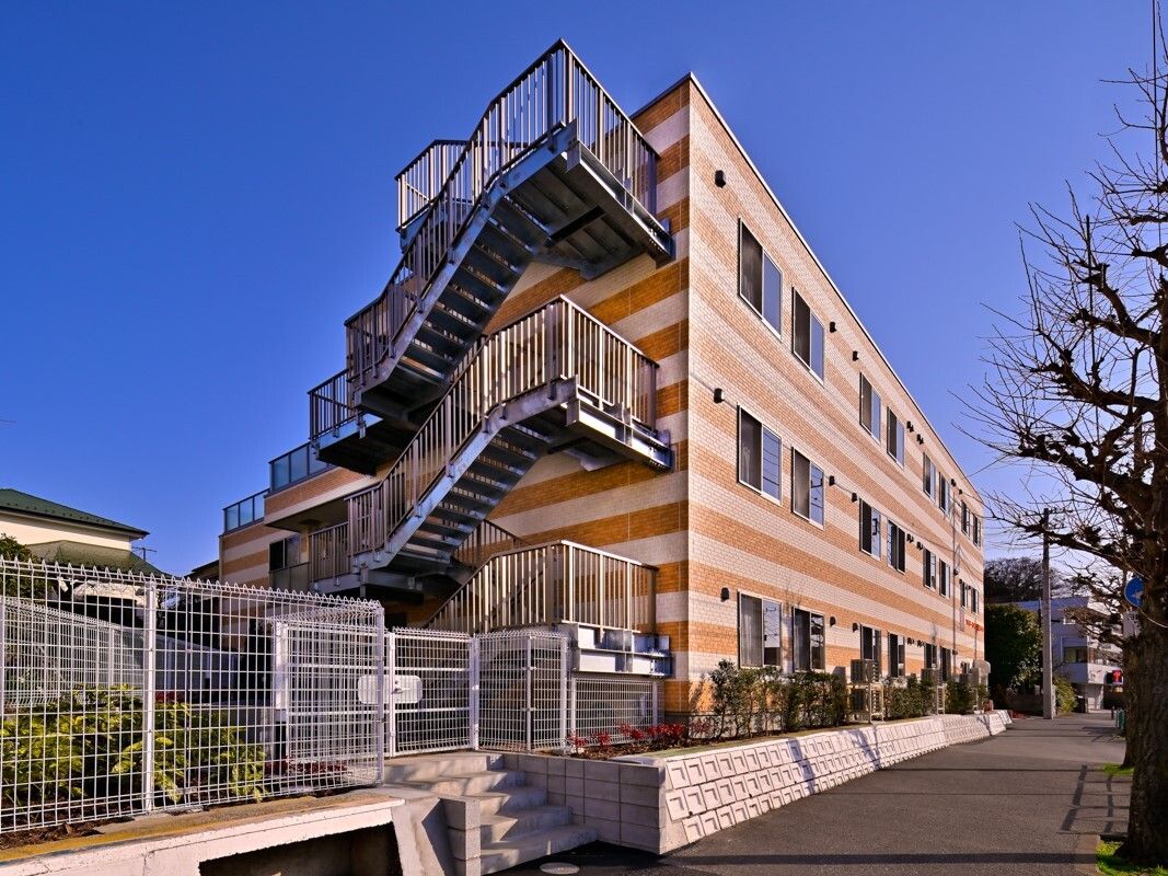 ストライプ柄の3階建ての建物には屋外階段が設置され、日当たりのいい場所に建っている。