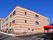 ストライプ柄の3階建ての建物の玄関には車寄せが付き、自動販売機が設置され、駐車場もある。