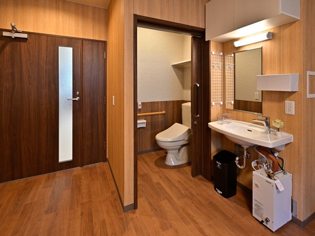 手すりや呼び出しボタンが設置されているトイレや車いす対応の洗面所が付いたフローリングの部屋。