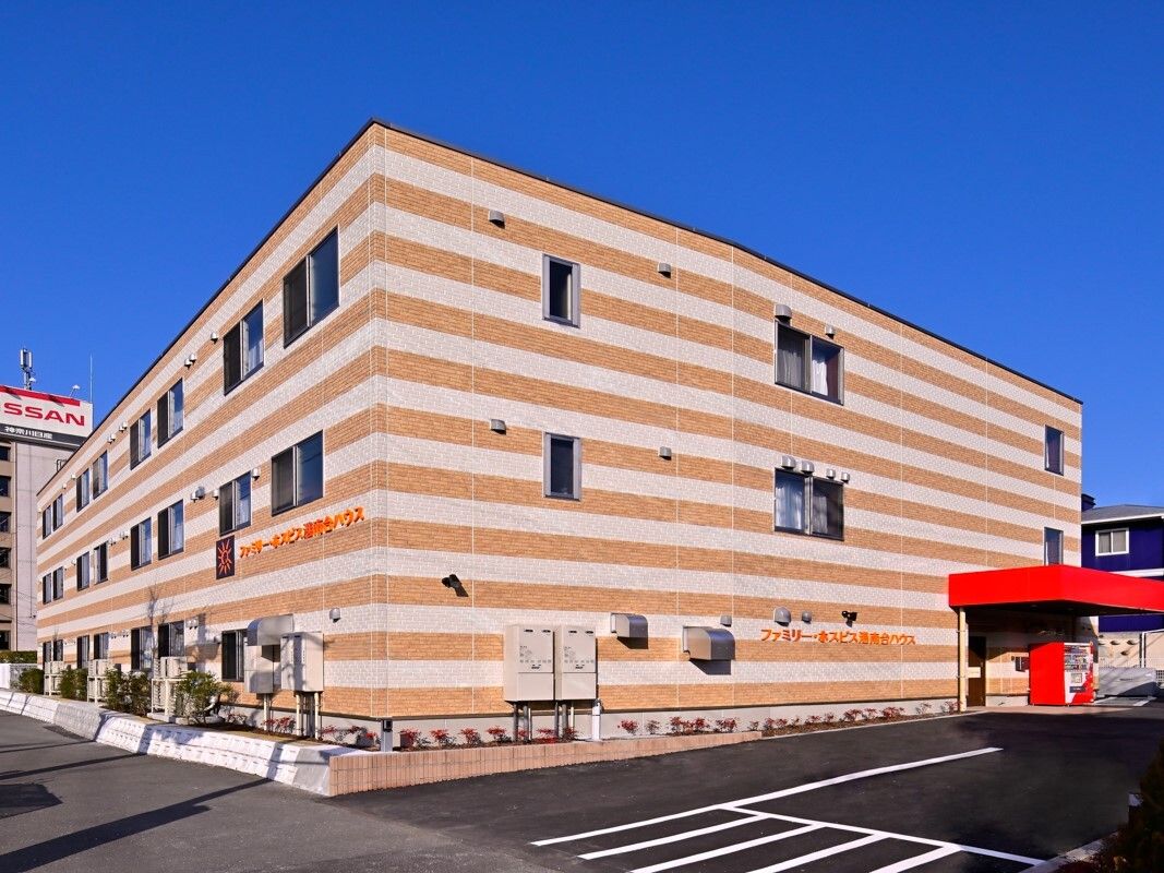 ストライプ柄の3階建ての建物のある敷地内には駐車場があり、日当たりのいい場所に建っている。