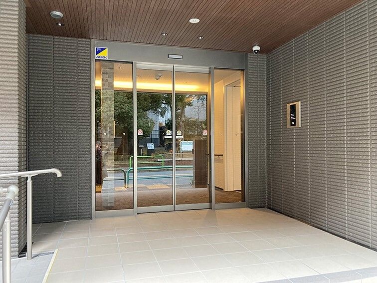 自動ドアが設置され、警備会社の大きなステッカーが貼られている玄関先には手すりも設置されている。