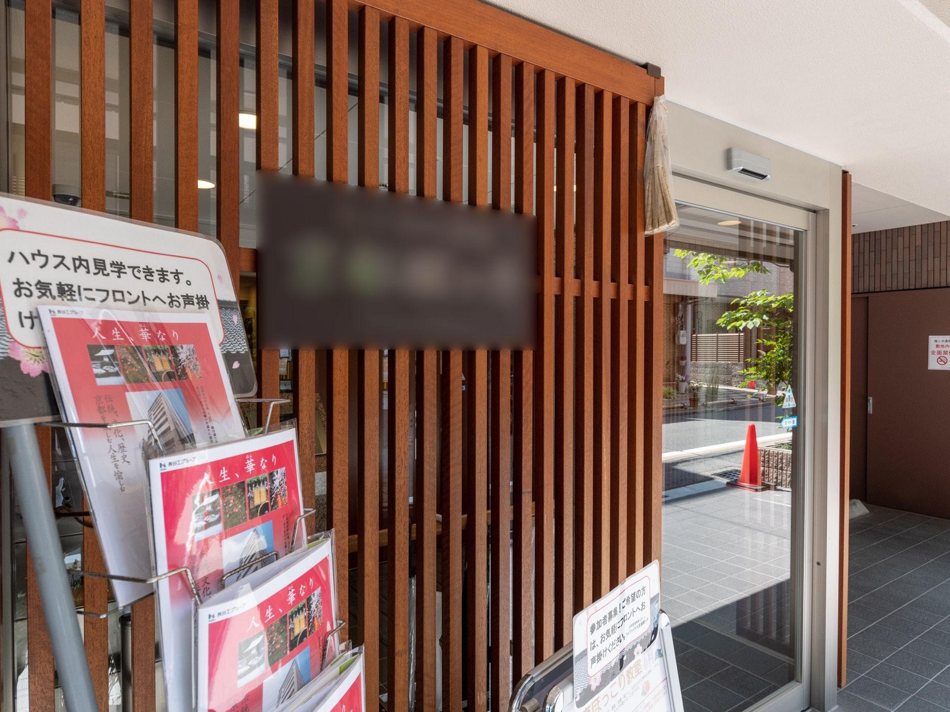 施設の看板はブラウンのプレートになっておりおしゃれな雰囲気になっている。看板のそばにはチラシが置かれている。
