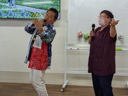 マイクを持って気持ちよさそうに歌っている人が２名。後ろにはカラオケの映像が映った大きなテレビがある。