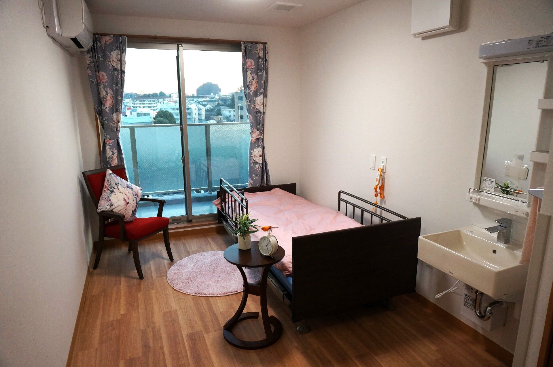 エアコンが付いたフローリングの部屋。介護ベッドがあり、ベッドサイドには緊急通報装置もある。