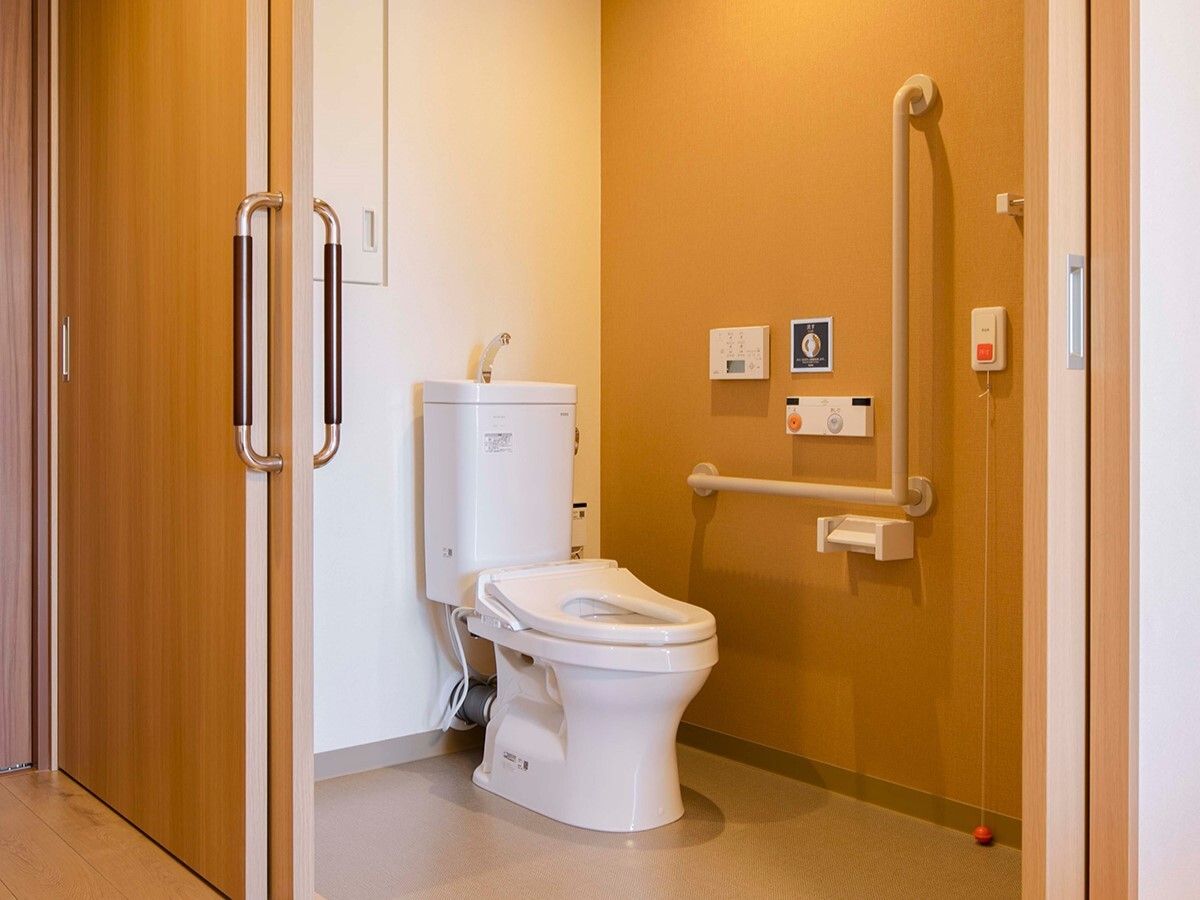 オレンジの呼び出しボタンや手すりが付いた広いトイレには、大きなドアが付いている。