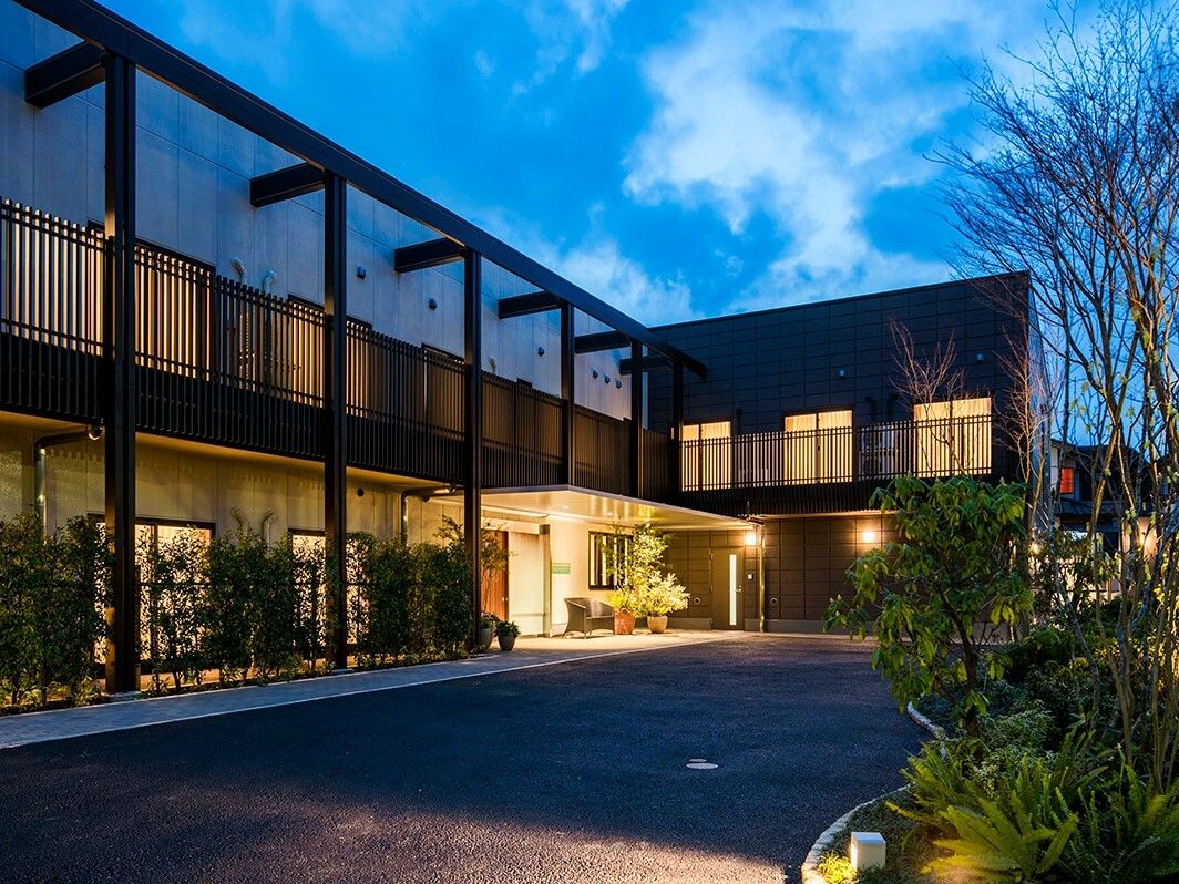 辺りが薄暗くなり、２階建ての建物は館内に照明が灯っている。敷地内には庭があり、草木が植えられている。