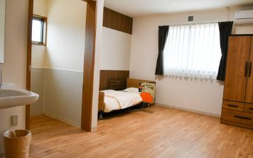 トイレや車いす対応の洗面所が付いたフローリングの部屋。介護ベッドやエアコンもある。