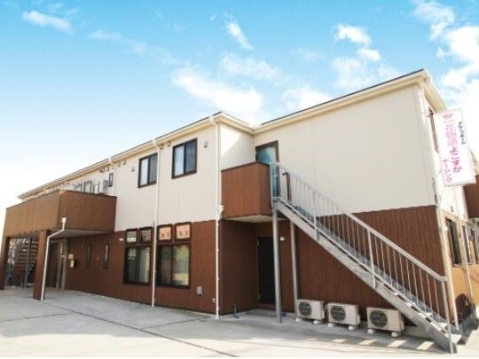 屋外階段を設置した２階建ての建物は日当たり良好でブラウンと白の外壁。2階にはベランダもある。