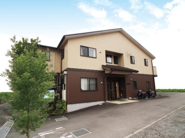 ２階建ての建物は玄関に屋根があり、三角屋根が付いている。駐車場には木も植えられている。