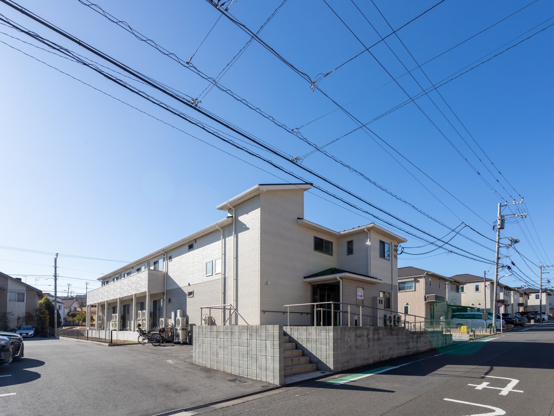白とブラウン系の２階建ての建物は玄関に手すり付きのスロープがあり、三角屋根が付いている。