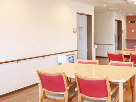 手すりが設置された食堂には赤い椅子がセットされたダイニングテーブルが複数ある。