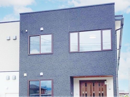 グレーと白の２階建ての建物は玄関に屋根があり大きな窓も付いている。