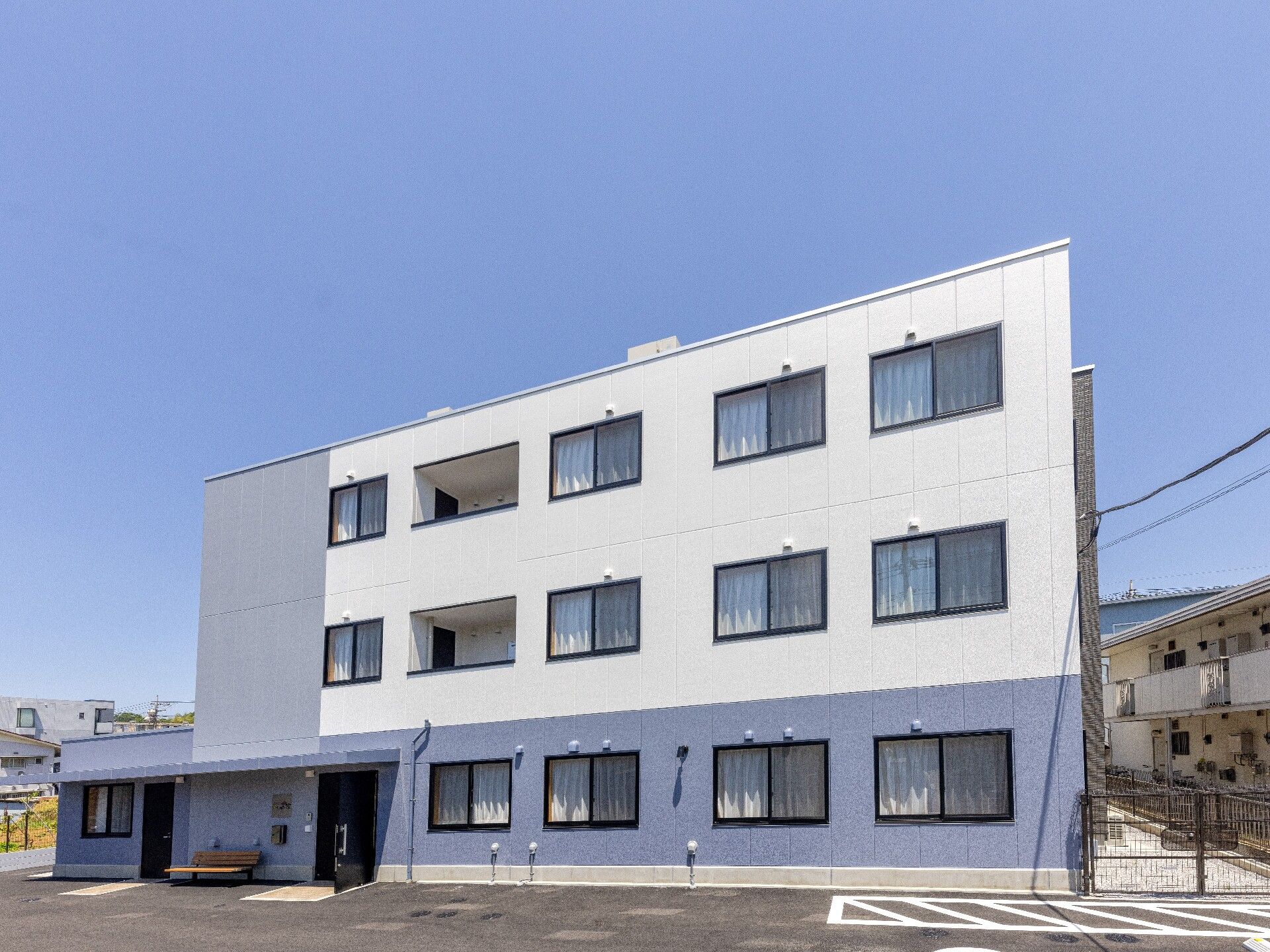 白とライトグレーの建物は3階建てで、駐車場も完備され、たくさんの窓が付いている。