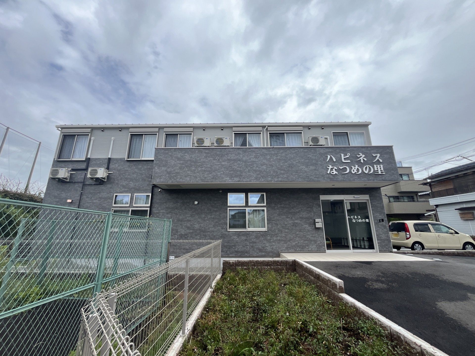 笑顔で誰かに手を振っている車いすの高齢女性とエプロンを付けた女性スタッフ。