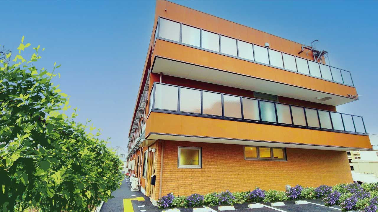 日当たりのいい場所に建っているブラウン系の３階建ての建物は横に長く、敷地内には駐車場もある。