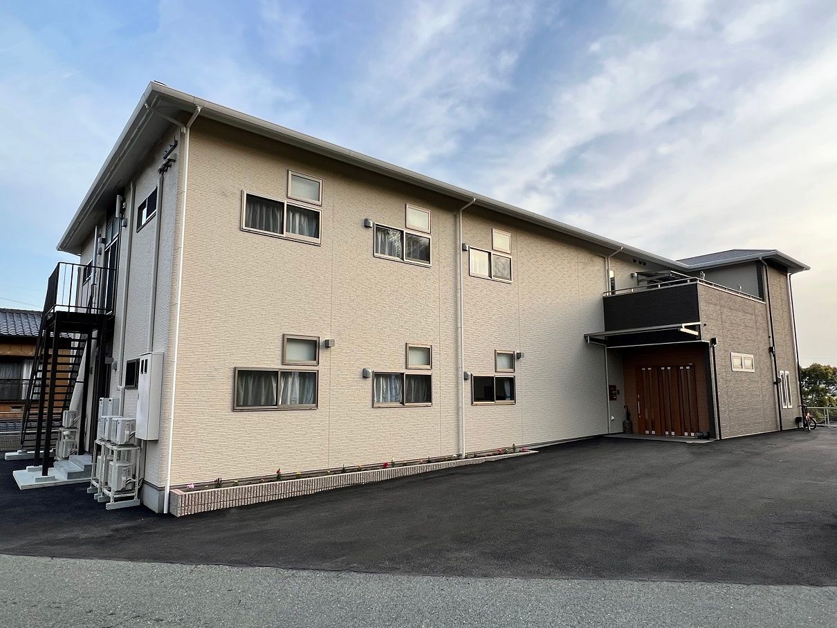 屋外階段が設置されたベージュの外壁の2階建ての建物。玄関には屋根が付いている。
