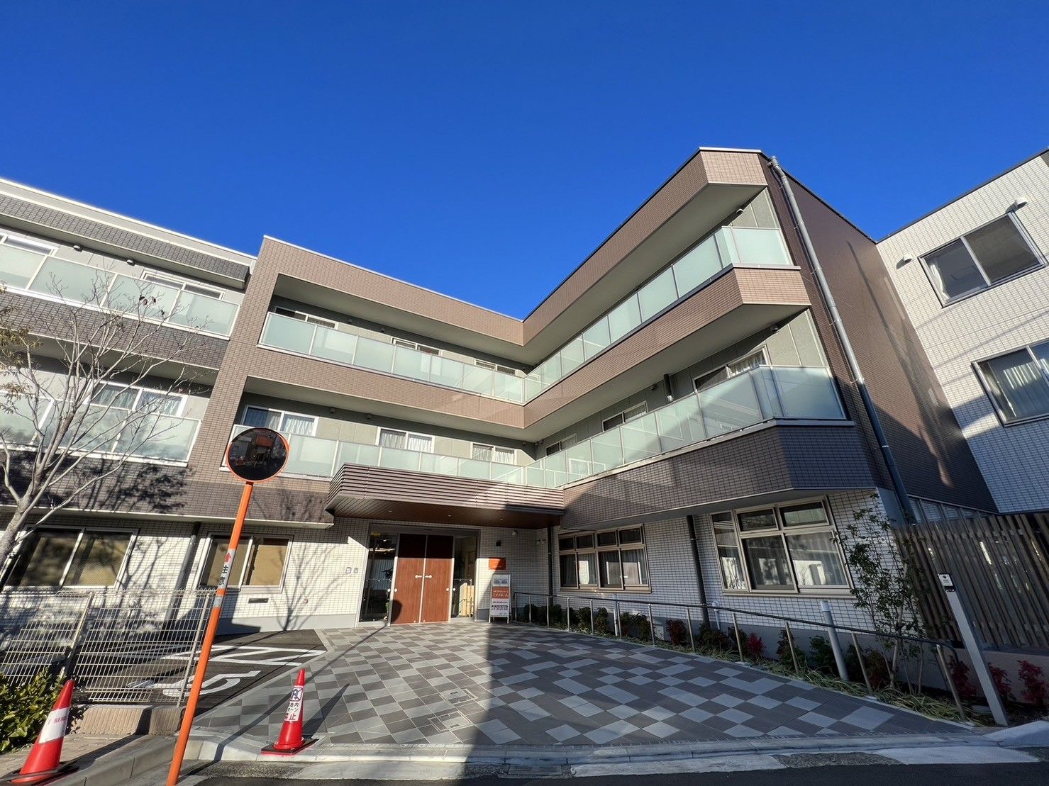 エル字型の3階建ての建物は日当たりのいい場所に建っている。敷地内には草木も植えられている。
